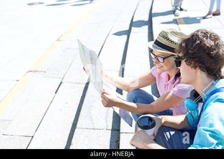 Heureux couple reading map while sitting on steps outdoors Banque D'Images