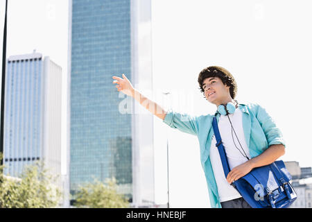 Jeune homme souriant saluant un taxi en ville Banque D'Images