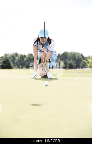 Jeune femme visant boule tout en s'agenouillant à golf course Banque D'Images