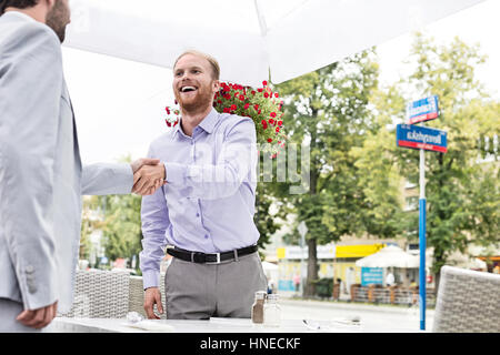 Happy businessmen shaking hands at outdoor restaurant Banque D'Images