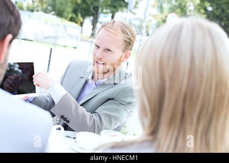 Businessman discussing over digital tablet avec des collègues at sidewalk cafe Banque D'Images