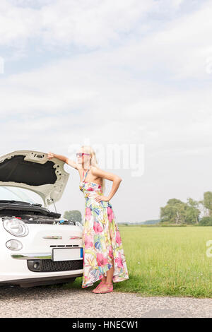 De toute la longueur tendue woman standing by broken down car on country road Banque D'Images