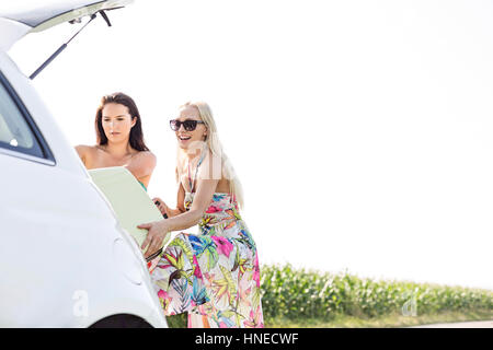 Happy female friends loading assurance dans coffre de voiture contre un ciel clair Banque D'Images