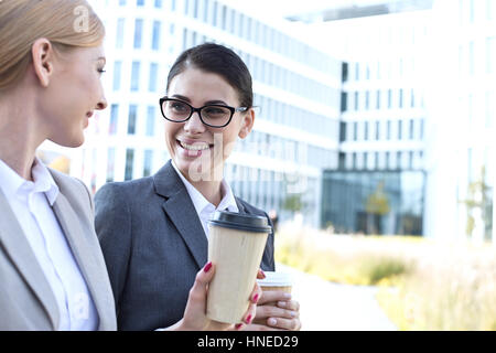 Les femmes d'affaires heureux de converser tout en maintenant des gobelets jetables en plein air Banque D'Images