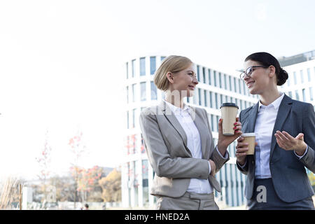 Les femmes d'affaires heureux de converser tout en maintenant des gobelets jetables outside office building Banque D'Images