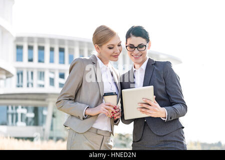 Heureux businesswomen using tablet PC outside office building Banque D'Images