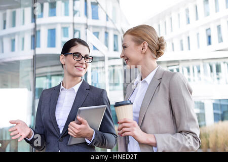 Les femmes d'affaires heureux avec tablet PC et gobelet jetable conversation outside office building Banque D'Images