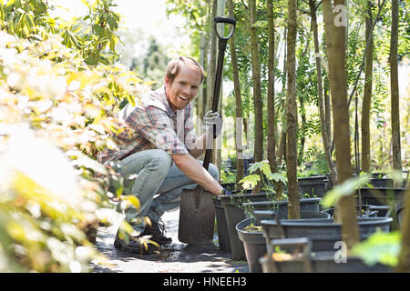 Portrait of happy gardener accroupi tout en maintenant à la pelle les pépinières Banque D'Images