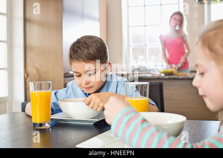 Frères et sœurs le petit-déjeuner à table avec mère de préparer des aliments en arrière-plan Banque D'Images