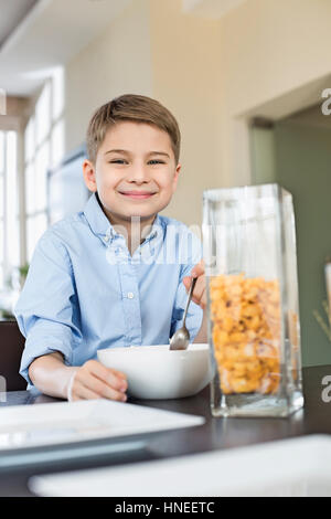 Portrait of smiling boy pouring flocons de maïs dans un bol à la maison Banque D'Images