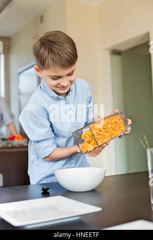 Smiling boy pouring flocons de maïs dans un bol à la maison Banque D'Images