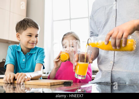 Portrait père servant jus d'orange pour les enfants dans la cuisine Banque D'Images