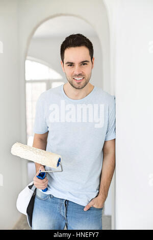 Portrait of handsome man holding paint roller in new house Banque D'Images