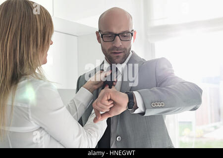 Mid adult businessman contrôle tout en montre-bracelet femme ajustant sa cravate à la maison Banque D'Images