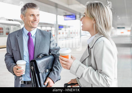 Businessman and businesswoman avec tasses à café à parler de la plate-forme ferroviaire Banque D'Images