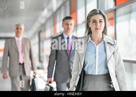 Belle jeune businesswoman walking avec des collègues masculins en arrière-plan à plate-forme du train Banque D'Images