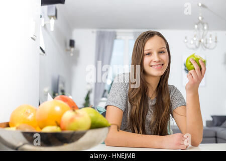 Portrait of smiling girl holding apple tout en étant assis à table dans la chambre Banque D'Images