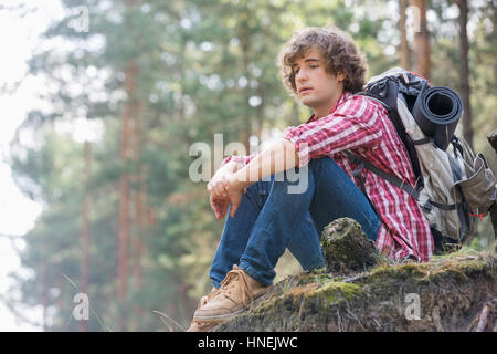 Toute la longueur de l'homme réfléchi backpacker détente sur falaise en forêt Banque D'Images