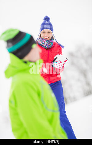 Smiling young woman having snowball fight avec ami masculin Banque D'Images