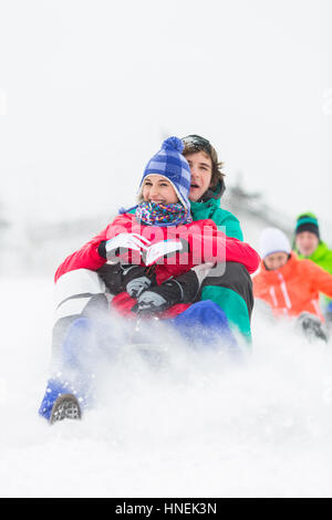 Jeunes amis excités Sledding in snow Banque D'Images