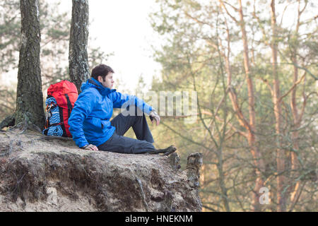 Vue latérale du randonneur assis sur le bord de la falaise en forêt Banque D'Images