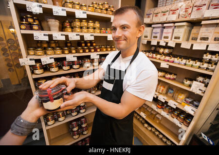 Vendeur donner pot de confiture à female customer in grocery store Banque D'Images