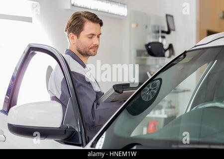 Vue latérale du technicien d'entretien d'hommes holding tablet PC lors de l'examen de voiture en atelier Banque D'Images