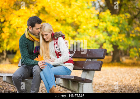 Jeune homme serrant femme timide sur banc de parc au cours de l'automne Banque D'Images