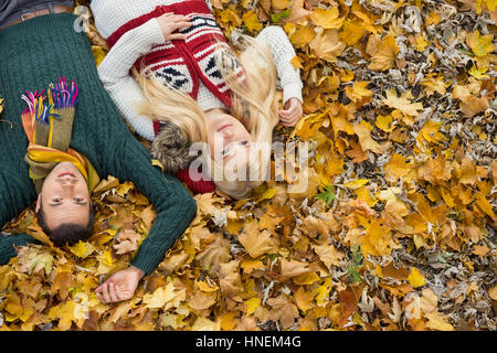 High angle portrait of young couple lying on autumn leaves at park Banque D'Images