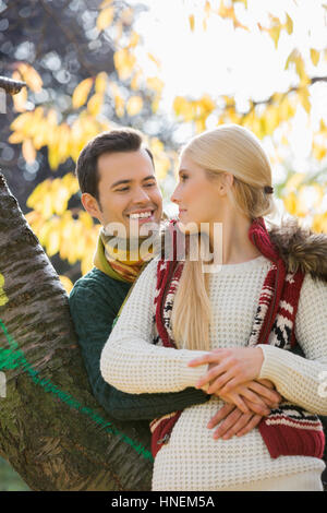 Happy young man hugging woman tout en s'appuyant sur tronc d'arbre au cours de l'automne dans le parc Banque D'Images