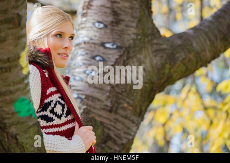 Young woman in vêtements chauds debout près des arbres dans le parc Banque D'Images