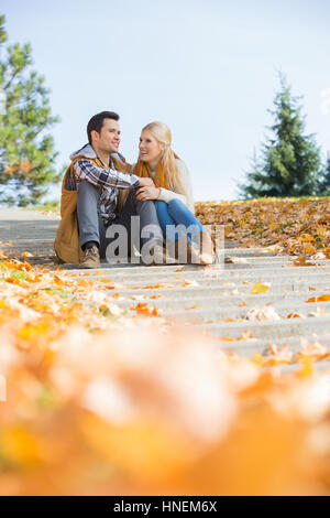 Happy young couple sitting on steps in park Banque D'Images