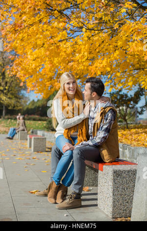 Heureux femme assise sur les genoux de l'homme au parc au cours de l'automne Banque D'Images