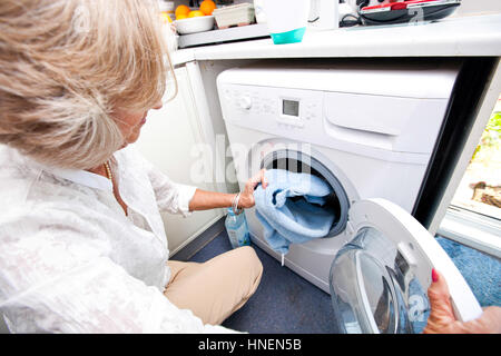 Senior woman loading towel en machine à laver à la maison Banque D'Images