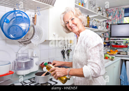 Portrait of senior woman pouring olive oil dans la casserole en cuisine domestique Banque D'Images