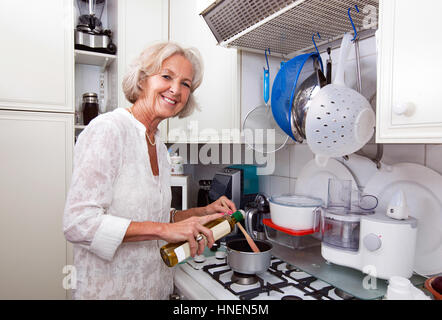 Portrait of senior woman ajout d'huile d'olive dans la casserole au comptoir de la cuisine Banque D'Images