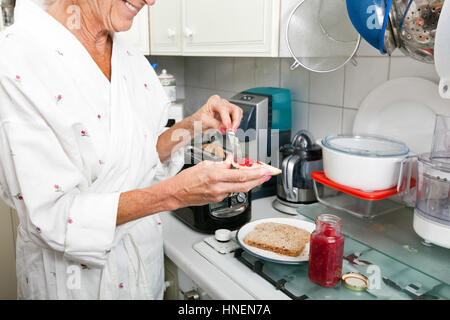 Portrait of senior woman l'application de la confiture sur du pain grillé dans la cuisine Banque D'Images