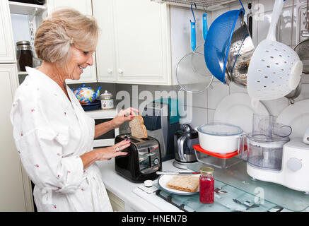 Happy senior woman preparing toast en cuisine domestique Banque D'Images