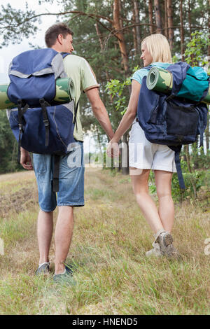 Vue arrière sur toute la longueur de jeunes backpackers holding hands in countryside Banque D'Images