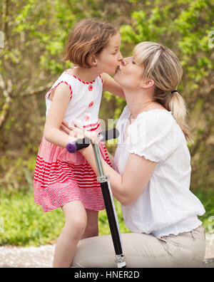 Mère et fille kissing in park with scooter Banque D'Images