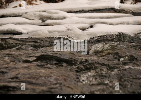 Close up de l'eau traversant un ruisseau gelé partiellement. Banque D'Images