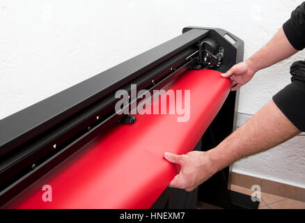 Mains de maître de l'impression grand format rouge chargement film sur plotter machine, close-up view incognito Banque D'Images