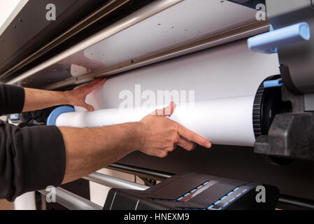 Close-up man chargement mains blanc grand format rouleau de papier sur l'imprimante professionnelle Banque D'Images