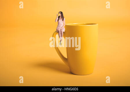 Le surréalisme avec design créatif. miniature Fille avec une tasse. La jeune fille dans une robe rose se trouve sur la tasse. Yellow tasse de thé ou de café. Jeune femme Banque D'Images