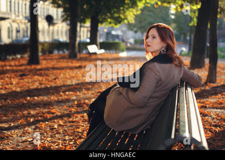 Belle femme aux cheveux rouges sur un banc dans le parc Banque D'Images