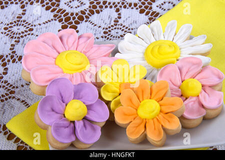 Accueil fantaisie faite de fleurs de printemps sugar cookies avec le glaçage royal sur fond de pétales. Servi sur une plaque carrée avec une serviette jaune en dessous. Banque D'Images