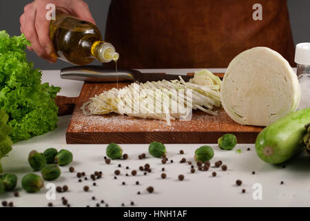 Close up of man's hands chou vinaigrette à l'huile. Les légumes vert placé sur une planche à découper en bois et surface blanche Banque D'Images