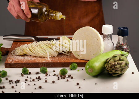 Puoring Chef de l'huile d'olive sur les légumes d'un placé sur une planche à découper en bois. Concept de suivre un régime Banque D'Images