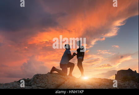 Silhouettes d'un homme faire de demande en mariage à sa petite amie sur le sommet de la montagne au coucher du soleil. Paysage avec silhouette d'amants contre s colorés Banque D'Images