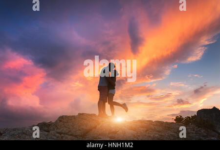 Silhouettes d'un homme embrasser et petite amie sur le sommet de la montagne au coucher du soleil. L'homme et de la femme. Paysage avec silhouette de personnes contre le col Banque D'Images